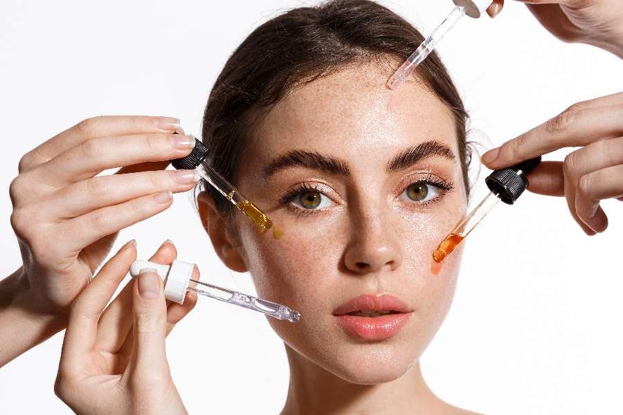 Beauty face of woman with freckles, natural clean and fresh glowing skin, apply anti aging collagen serum. Hands holding serum with active botanical ingredients vitamin c in dropper, white background