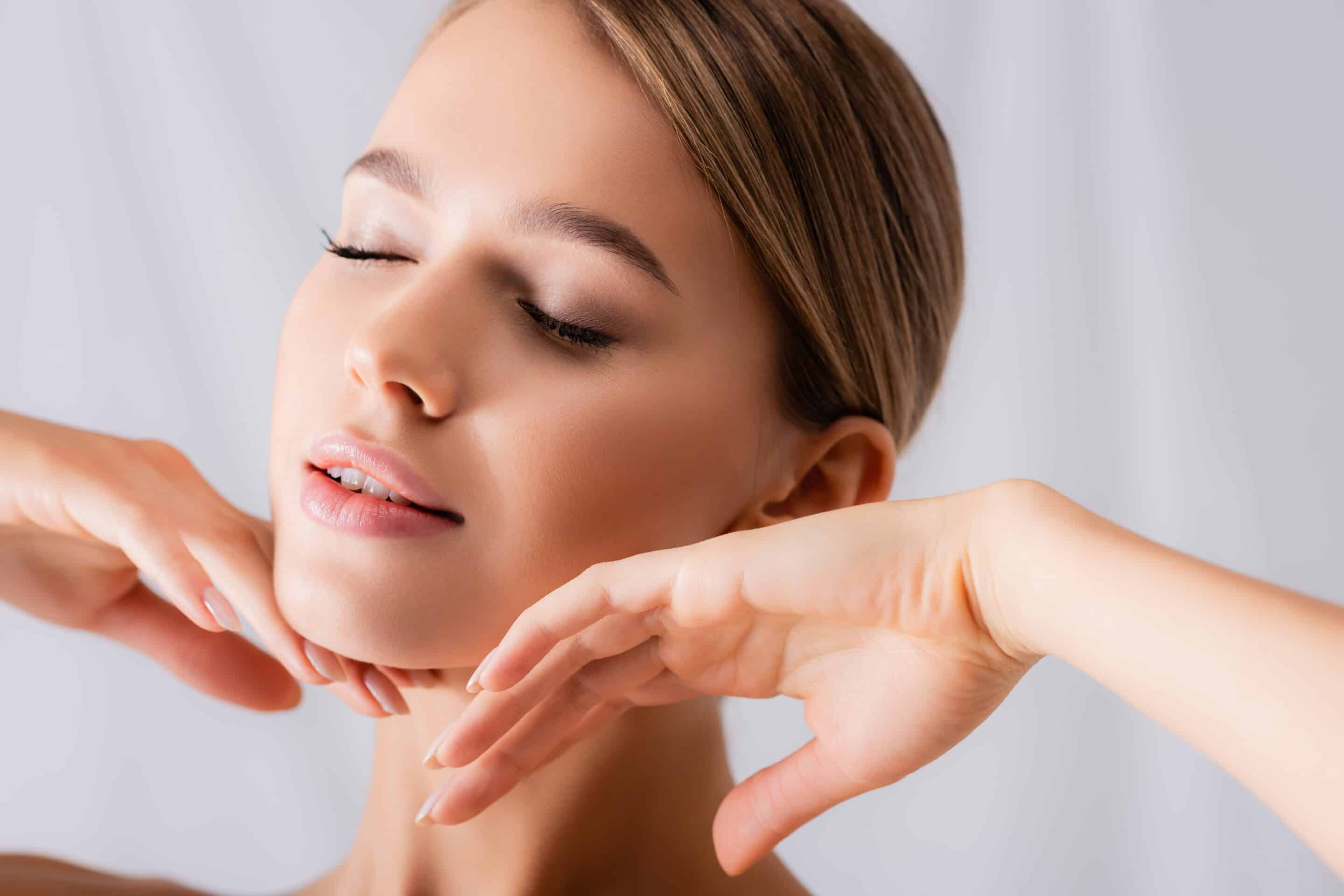 young woman with closed eyes touching face on white